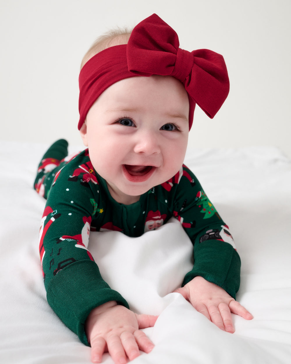 Baby wearing the Holiday Red Luxe Bow Headband with the Santa's Grooves Zippy