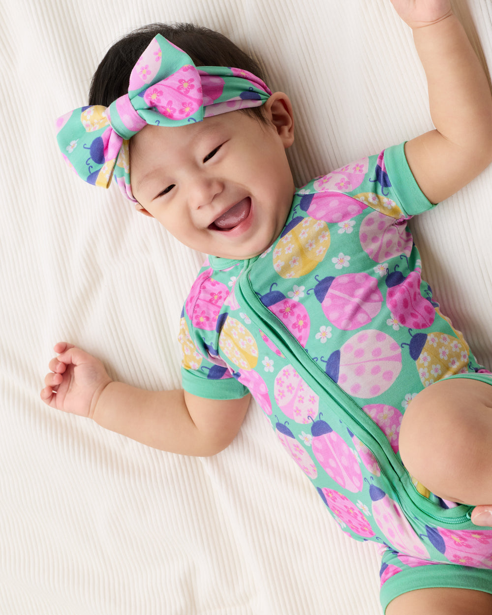 Child laying on a white blanket wearing the Ladybug Meadow Luxe Bow Headband