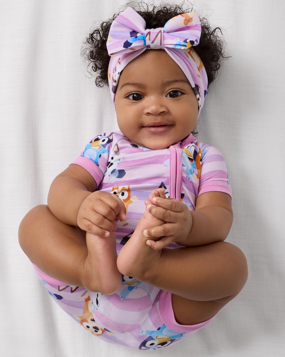 Aerial view of baby wearing the Pink Bluey Dance All Day Luxe Bow Headband and short sleeve zipper pajamas