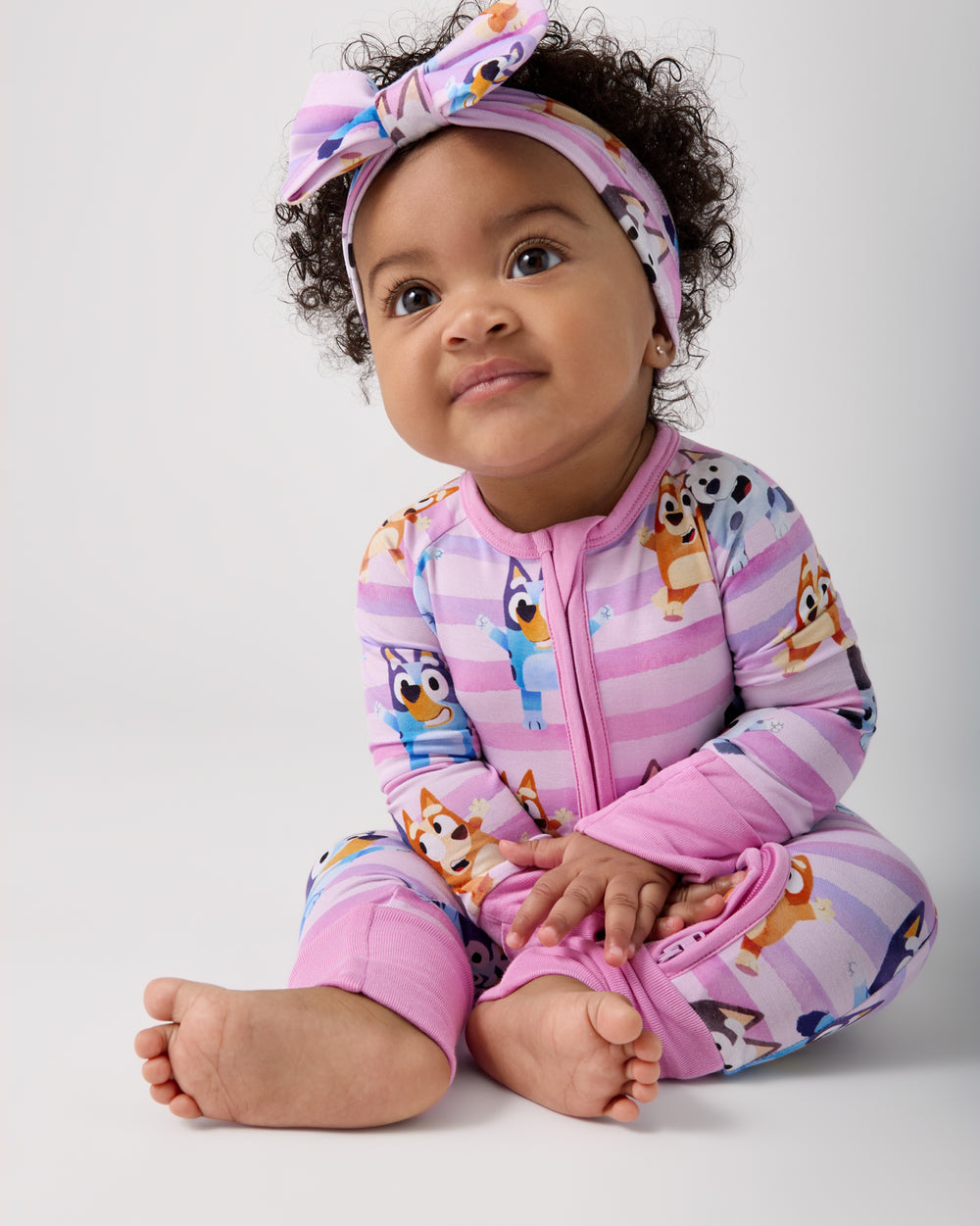 Sitting baby wearing the Pink Bluey Dance All Day Zippy and coordinating bow headband