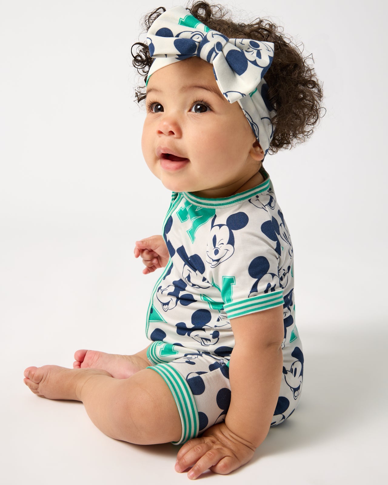 Sitting baby wearing the Disney Varsity Mickey Mouse Shorty Zippy and Luxe Bow Headband