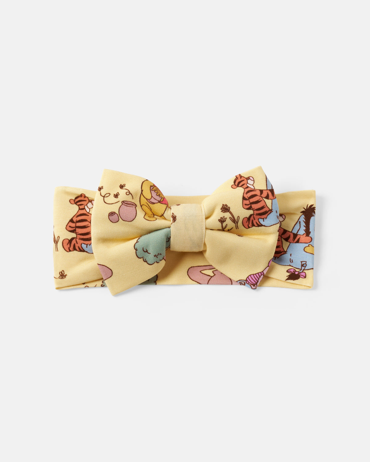 A pale yellow fabric bow tie with a matching elastic headband, featuring a colorful cartoon print of Winnie the Pooh and Tigger, set against a plain light gray background.