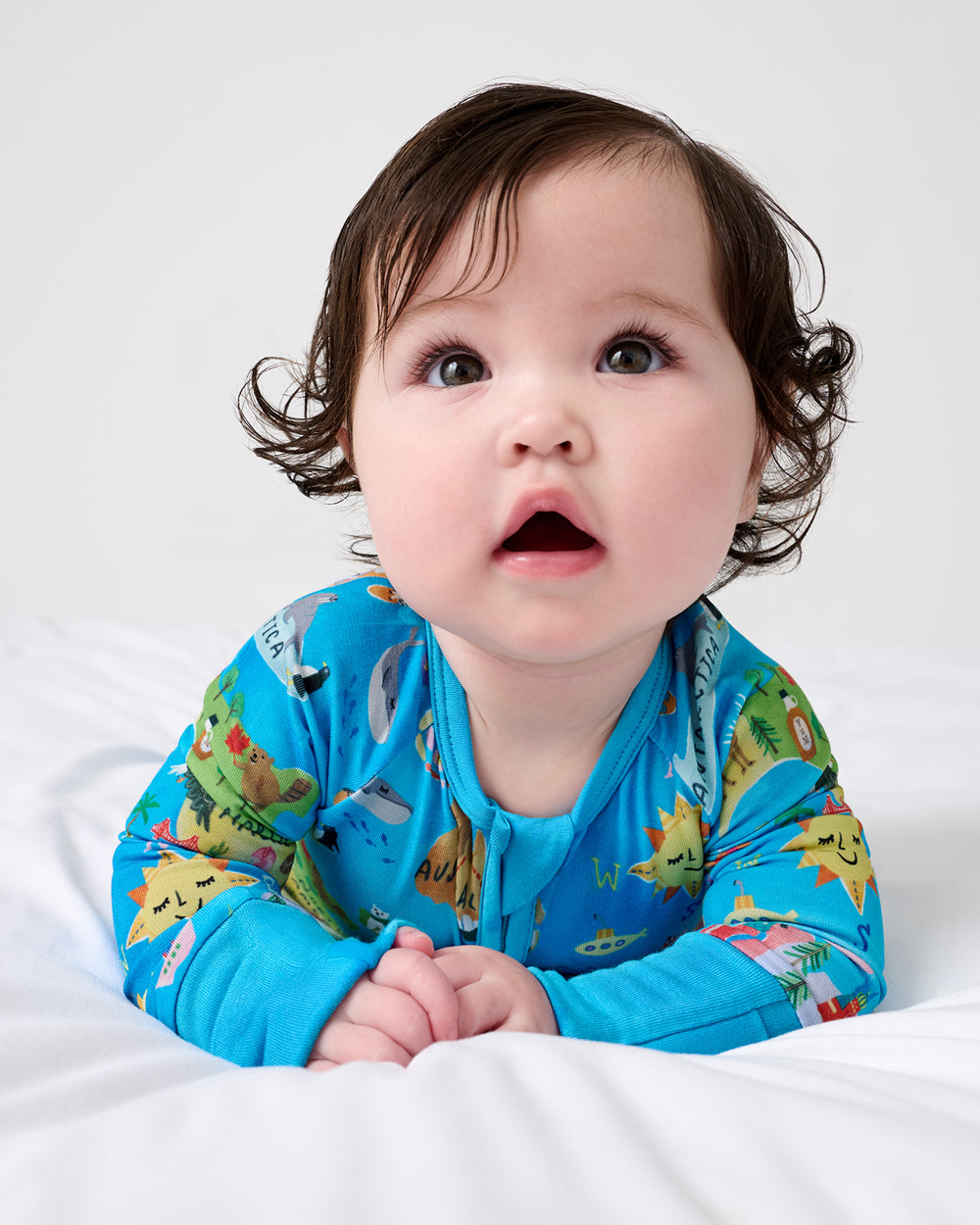 Baby laying on a white blanket wearing the Around The World Zippy