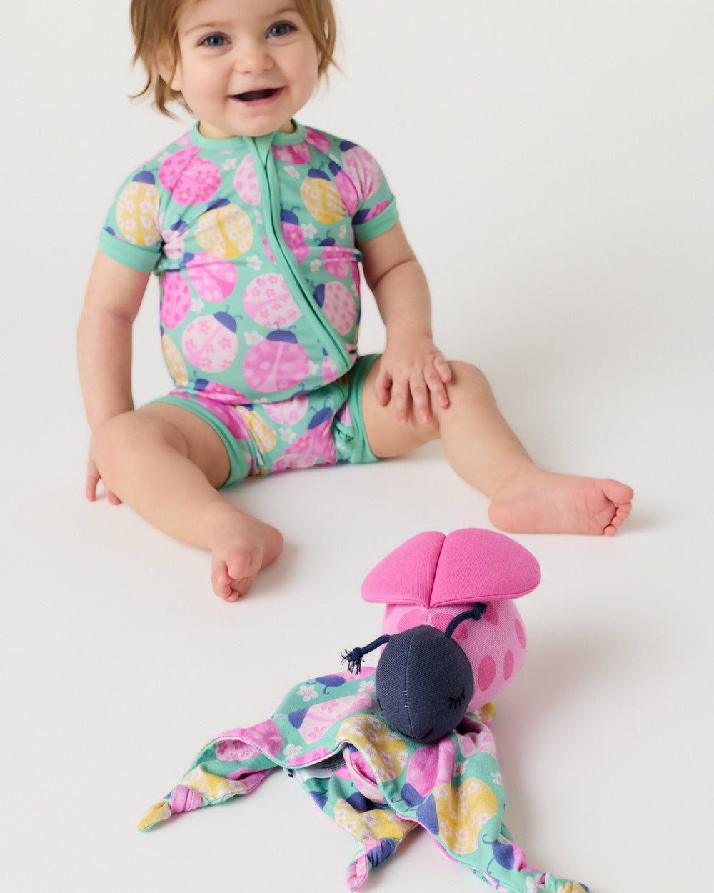 Child sitting on a white floor with the Rosie the Ladybug Sleepyhead Lovey in the foreground