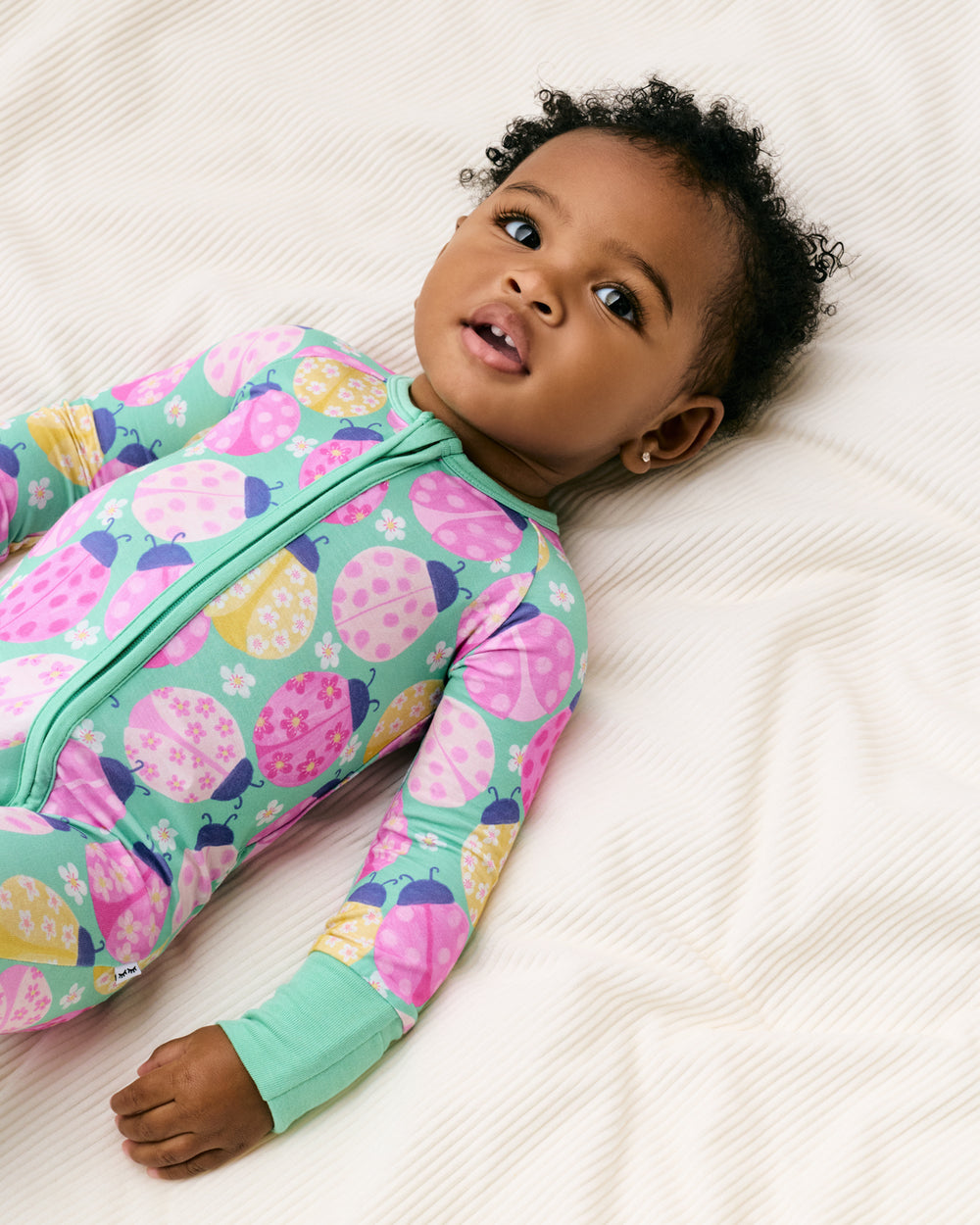 Child laying on a white blanket wearing the Ladybug Meadow Zippy