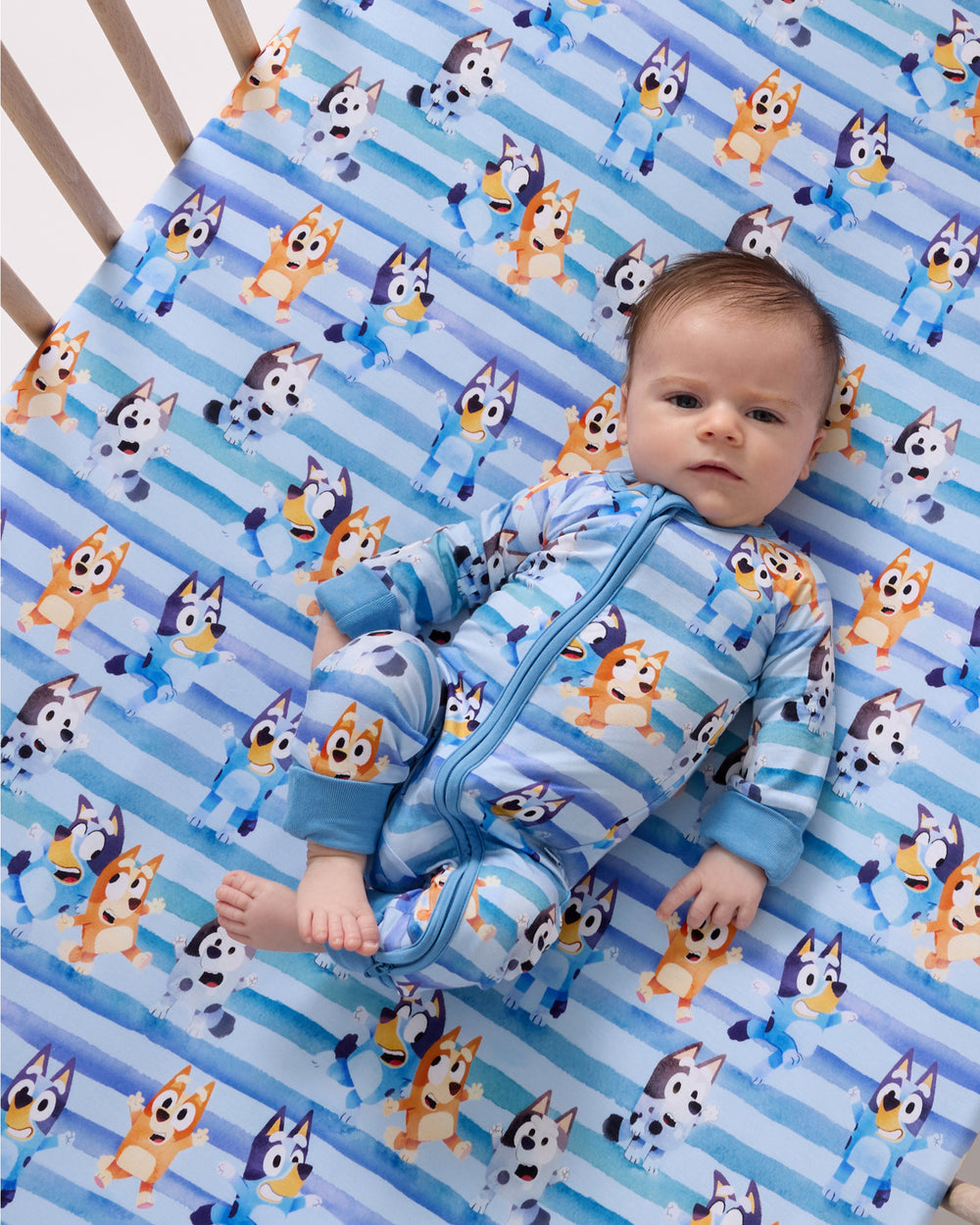 Alternate of baby laying on the Bluey Dance All Day Fitted Crib Sheet in a matching zippy