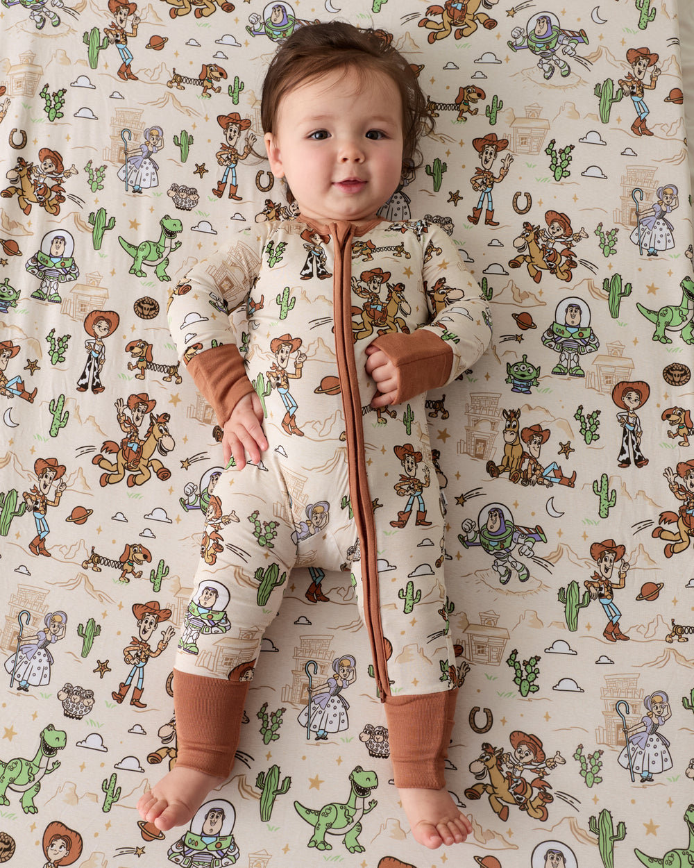 Aerial view of baby laying on the Disney & Pixar Woody's Wild West Fitted Crib Sheet in a matching zippy