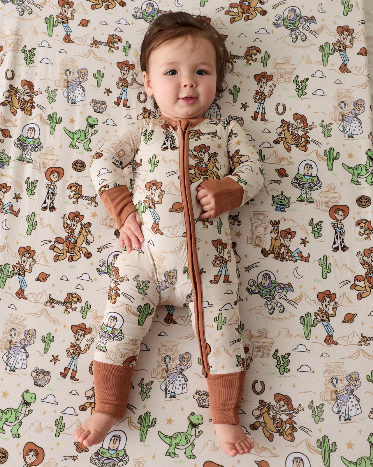 Aerial view of baby laying on the Disney & Pixar Woody's Wild West Fitted Crib Sheet in a matching zippy