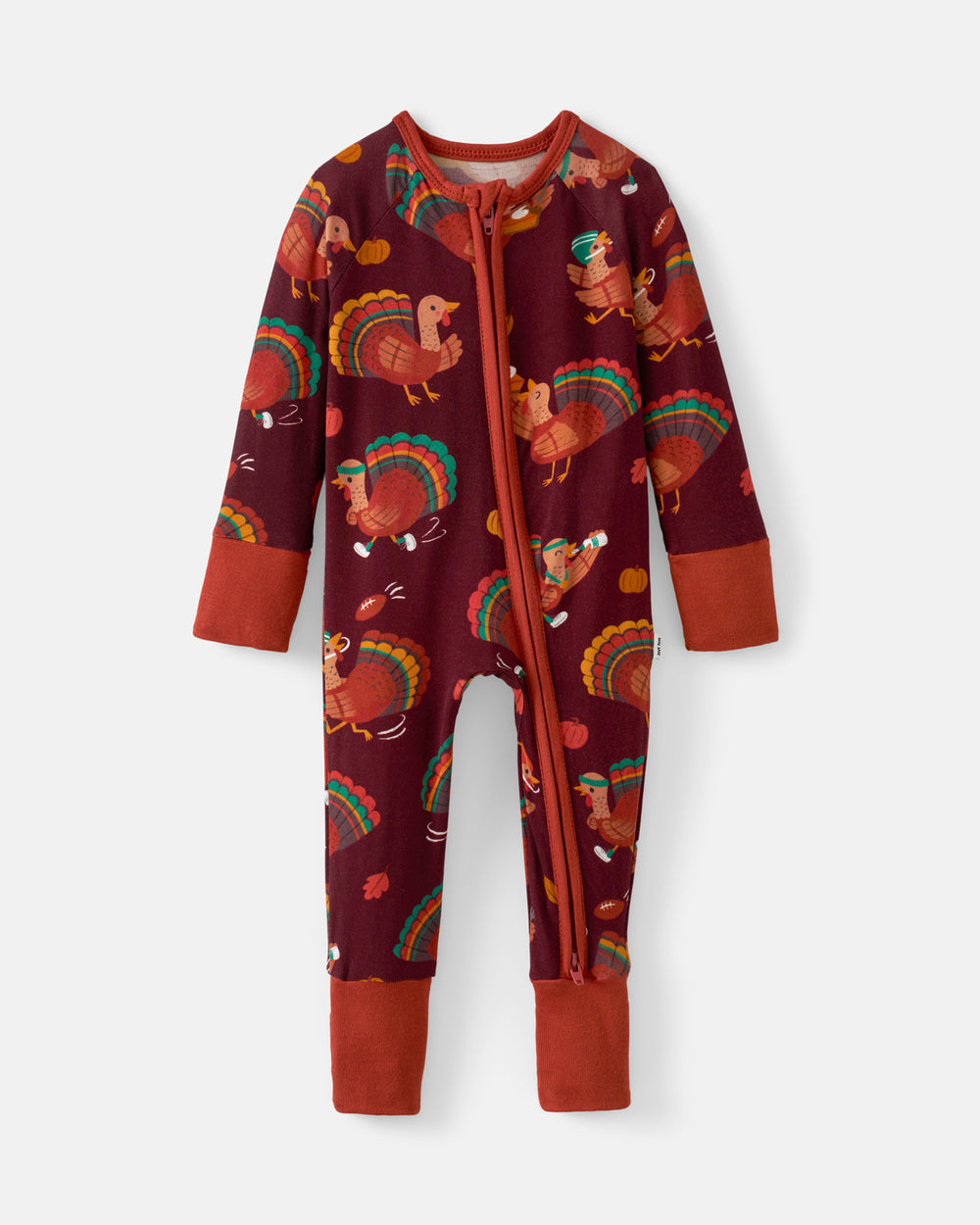 A baby's long-sleeve zip-up footed sleeper in a dark burgundy fabric with a colorful Thanksgiving turkey print, featuring rust-orange cuffs and footy cuffs.