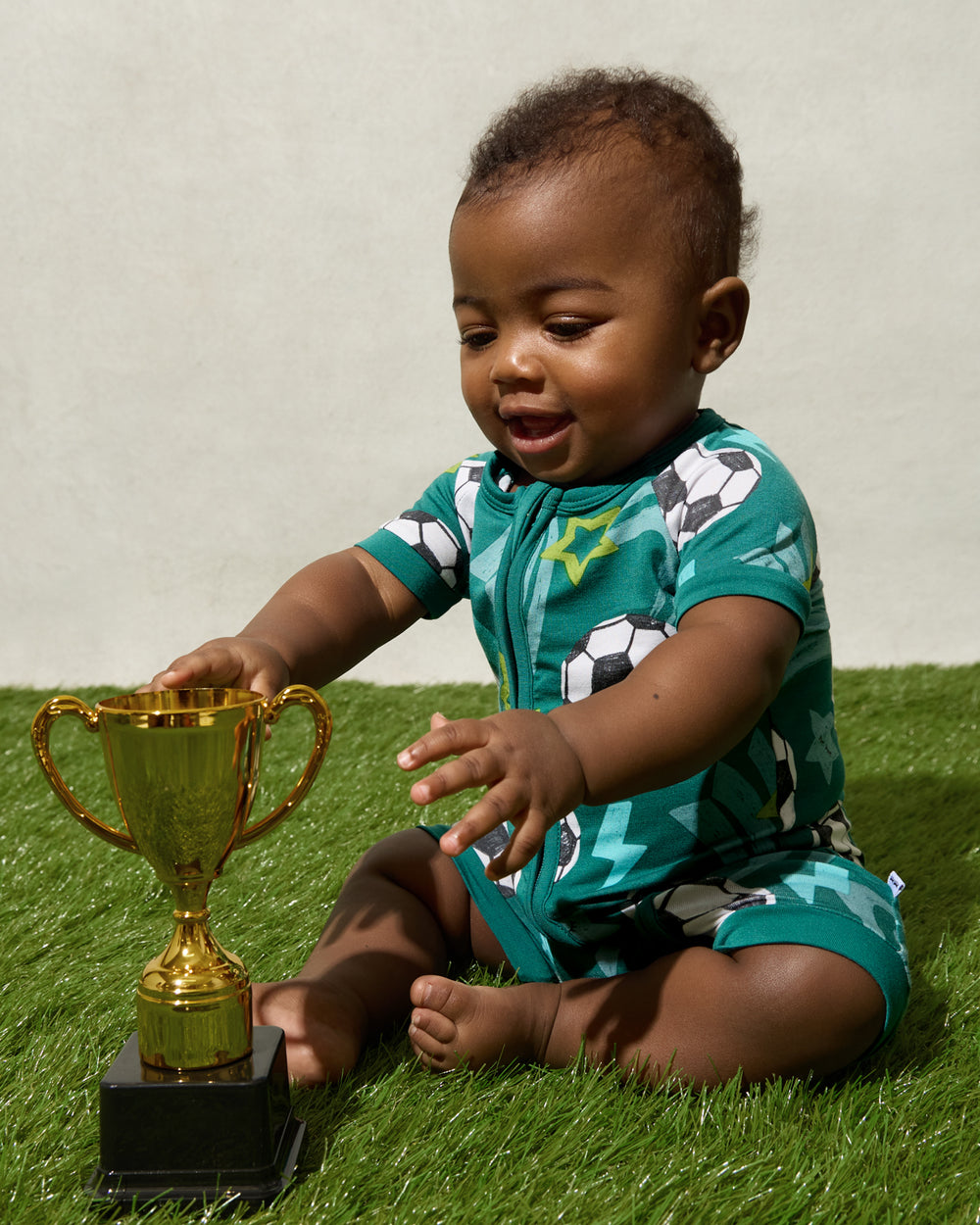 Newborn wearing the Soccer Stars Shorty Zippy sitting with a trophy