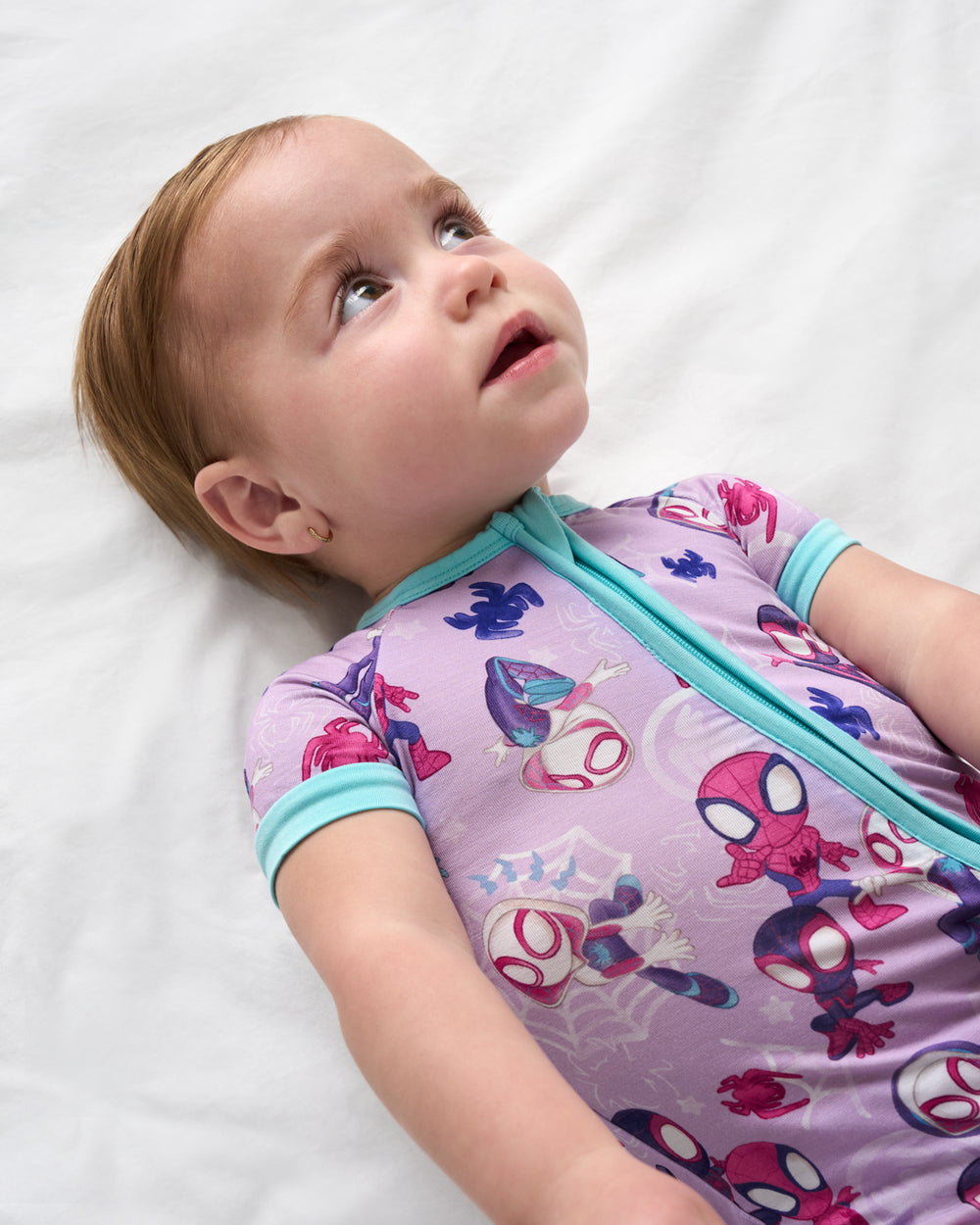 Baby laying on a white blanket wearing the Spidey & Friends Tiny Webs Shorty Zippy