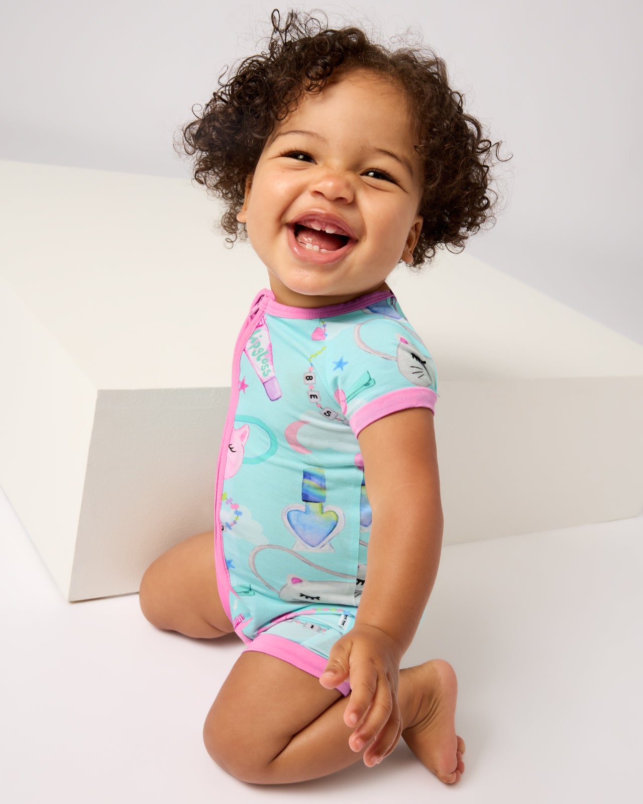 Kneeling baby wearing the Slumber Club Shorty Zippy