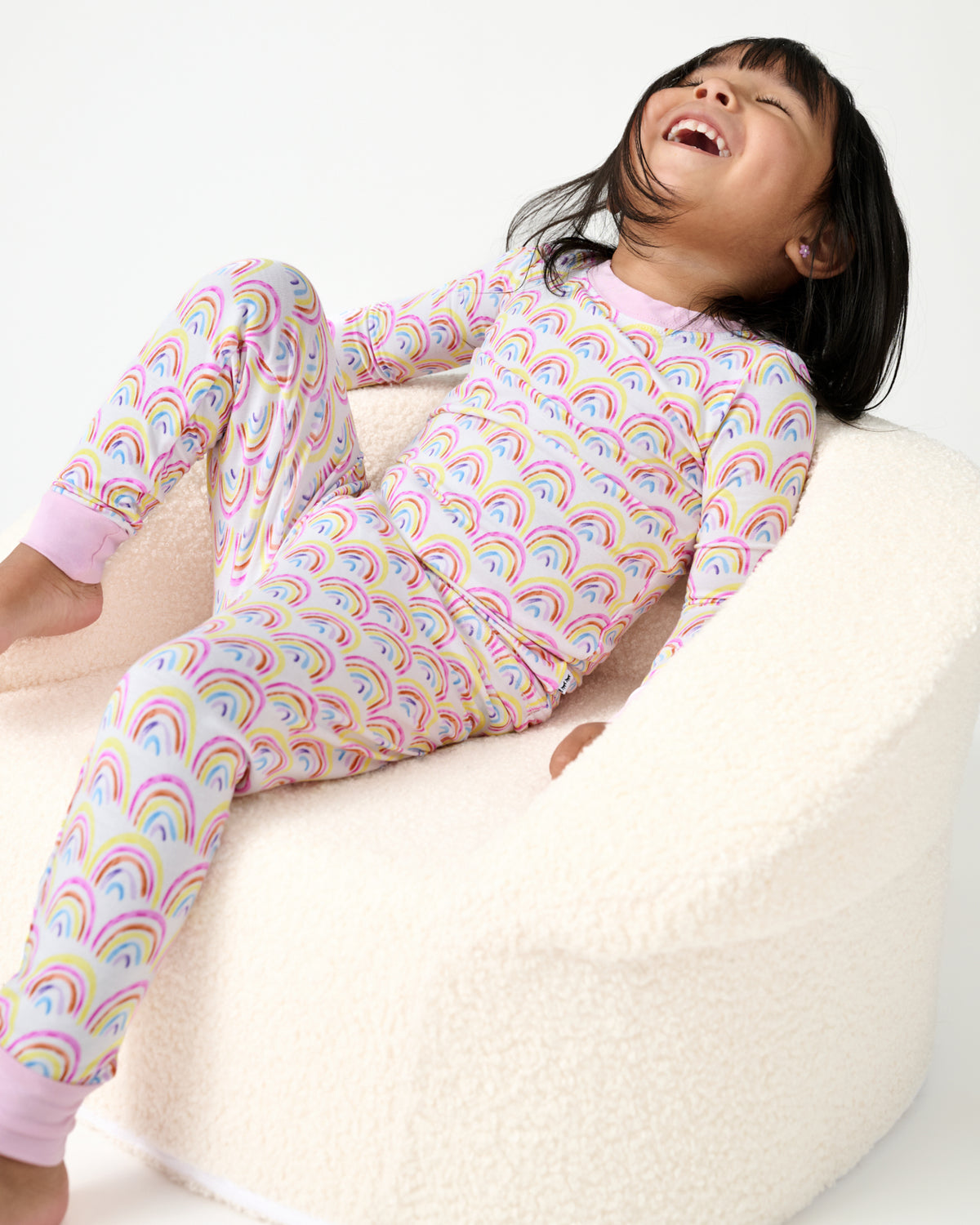 Girl sitting on a boucle chair wearing the Pastel Rainbows Two-Piece Pajama Set