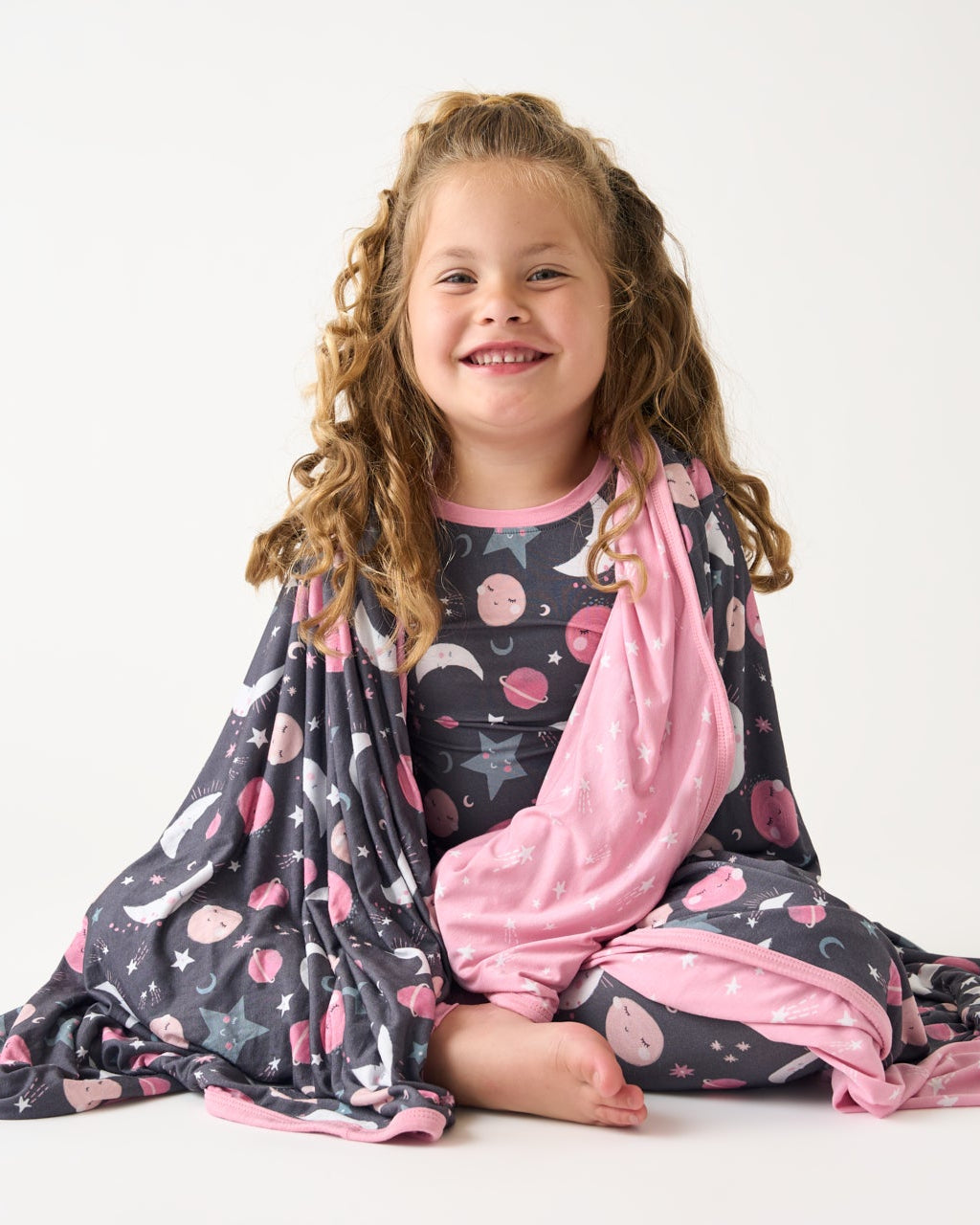 Sitting girl with the Pink To the Moon & Back Large Cloud Blanket® draped over her 