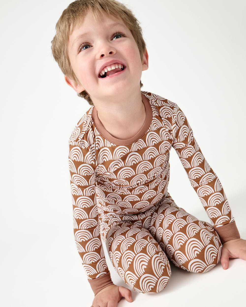 Sitting boy wearing the Rust Rainbows Two-Piece Pajama Set