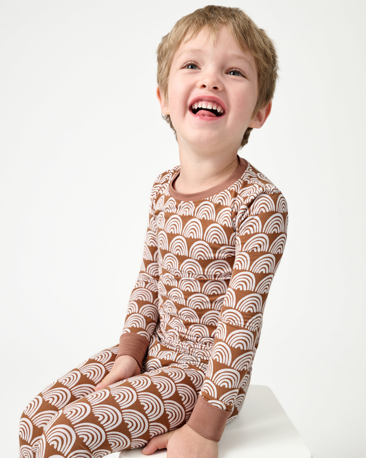 Close up of sitting child wearing the Rust Rainbows Two-Piece Pajama Set