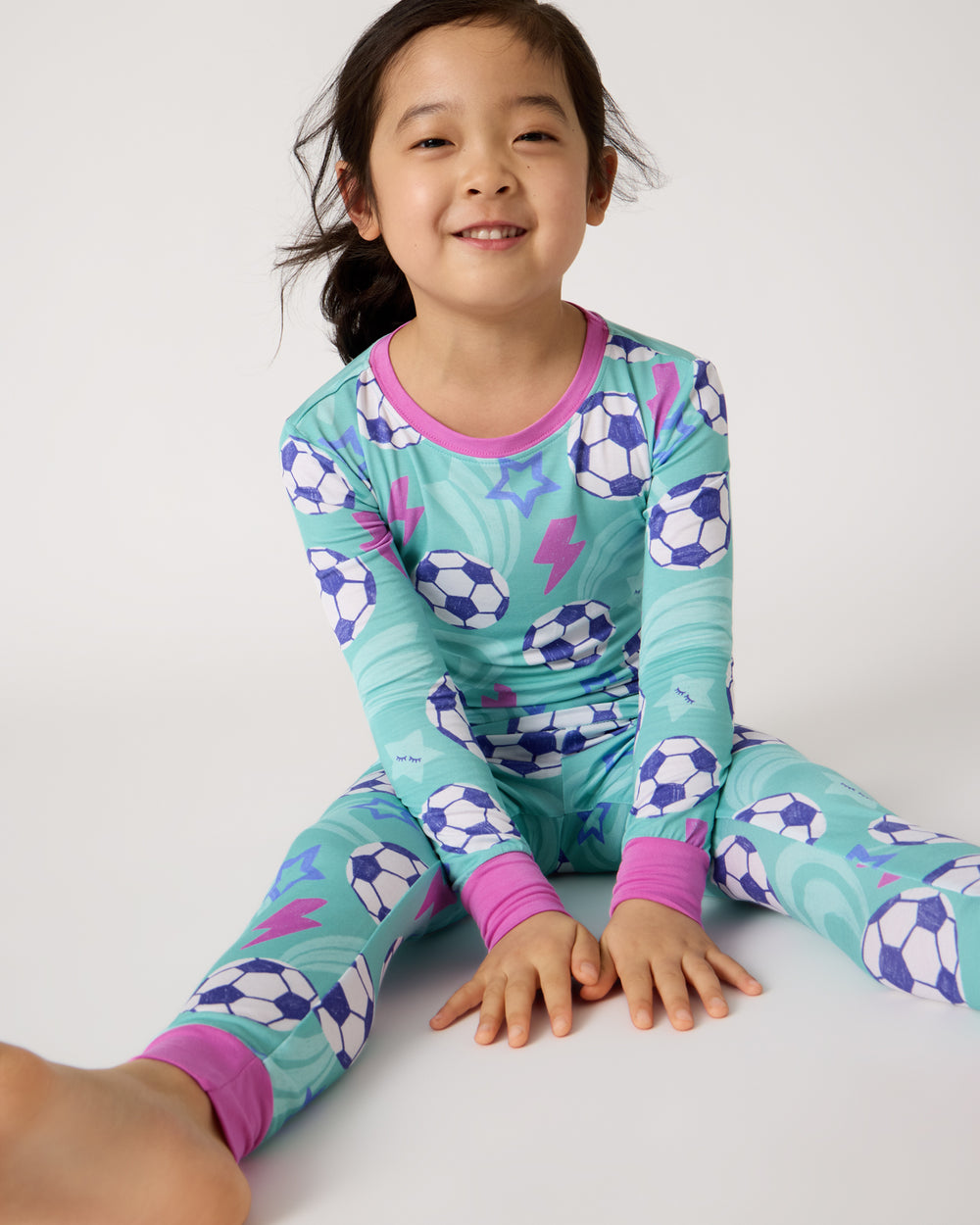 Sitting girl wearing the Aqua Soccer Stars Two-Piece Pajama Set
