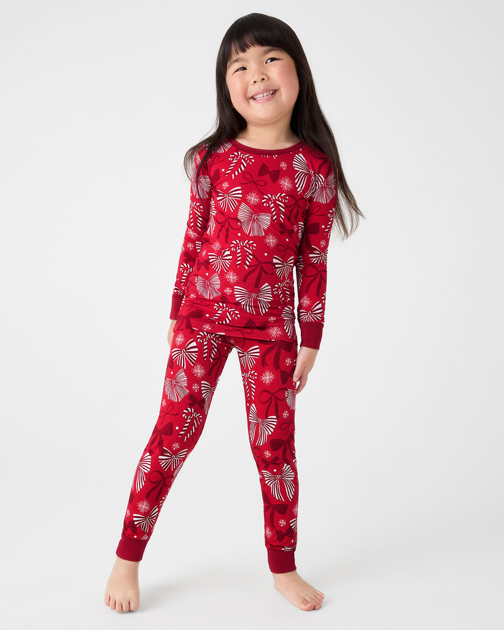 Standing child wearing the Holiday Bows Two-Piece Pajama Set