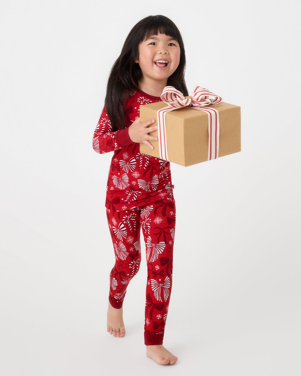 Girl holding a wrapped gift wearing the Holiday Bows Two-Piece Pajama Set