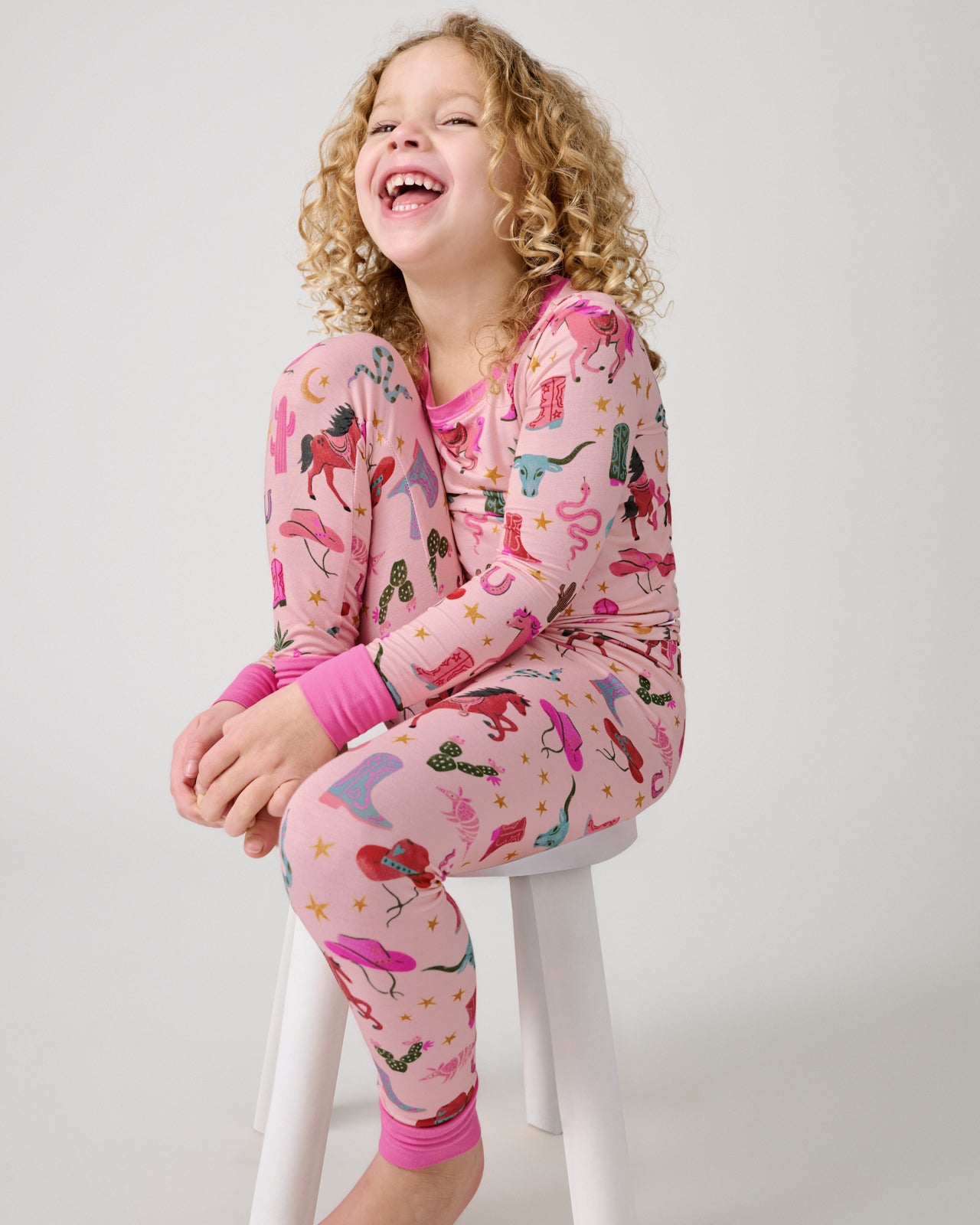 Girl sitting on a white stool in the Pink Rancher Roundup Two-Piece Pajama Set