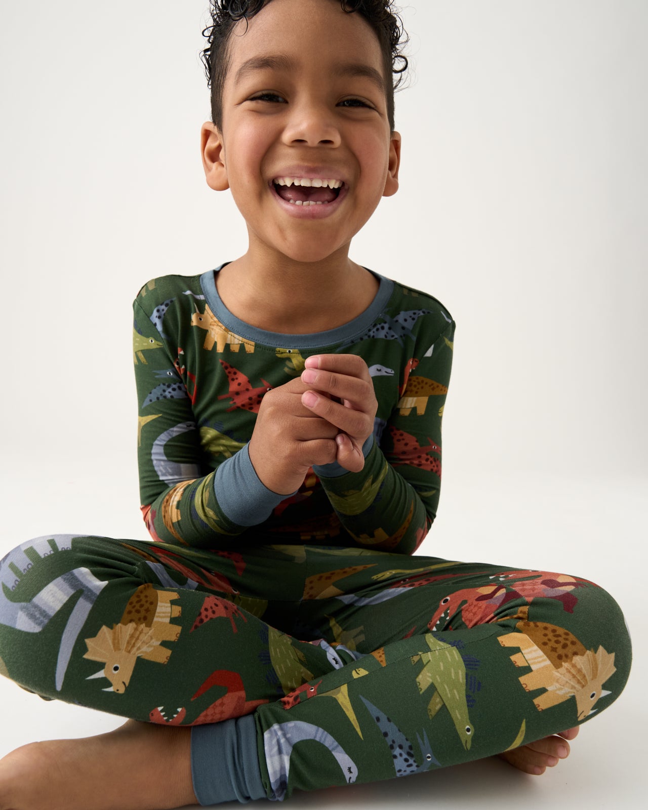 Sitting child wearing the Green Roar & Explore Two-Piece Pajama Set