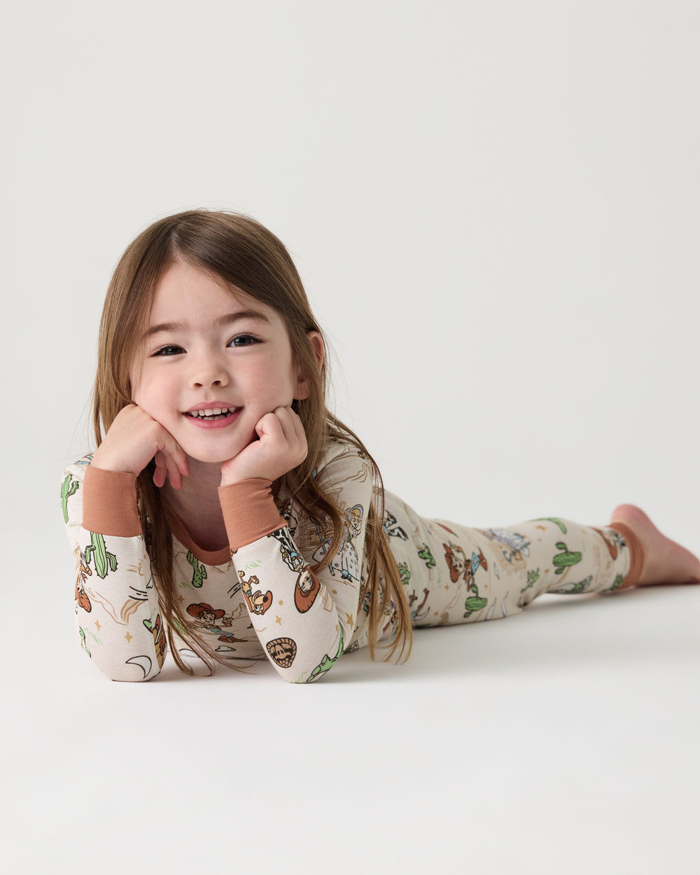 Child laying on a white surface wearing the Disney & Pixar Woody's Wild West Two-Piece Pajama Set