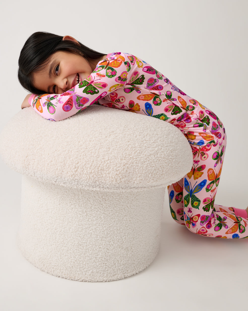Girl resting on a boucle ottoman wearing the Flutter Garden Two-Piece Pajama Set