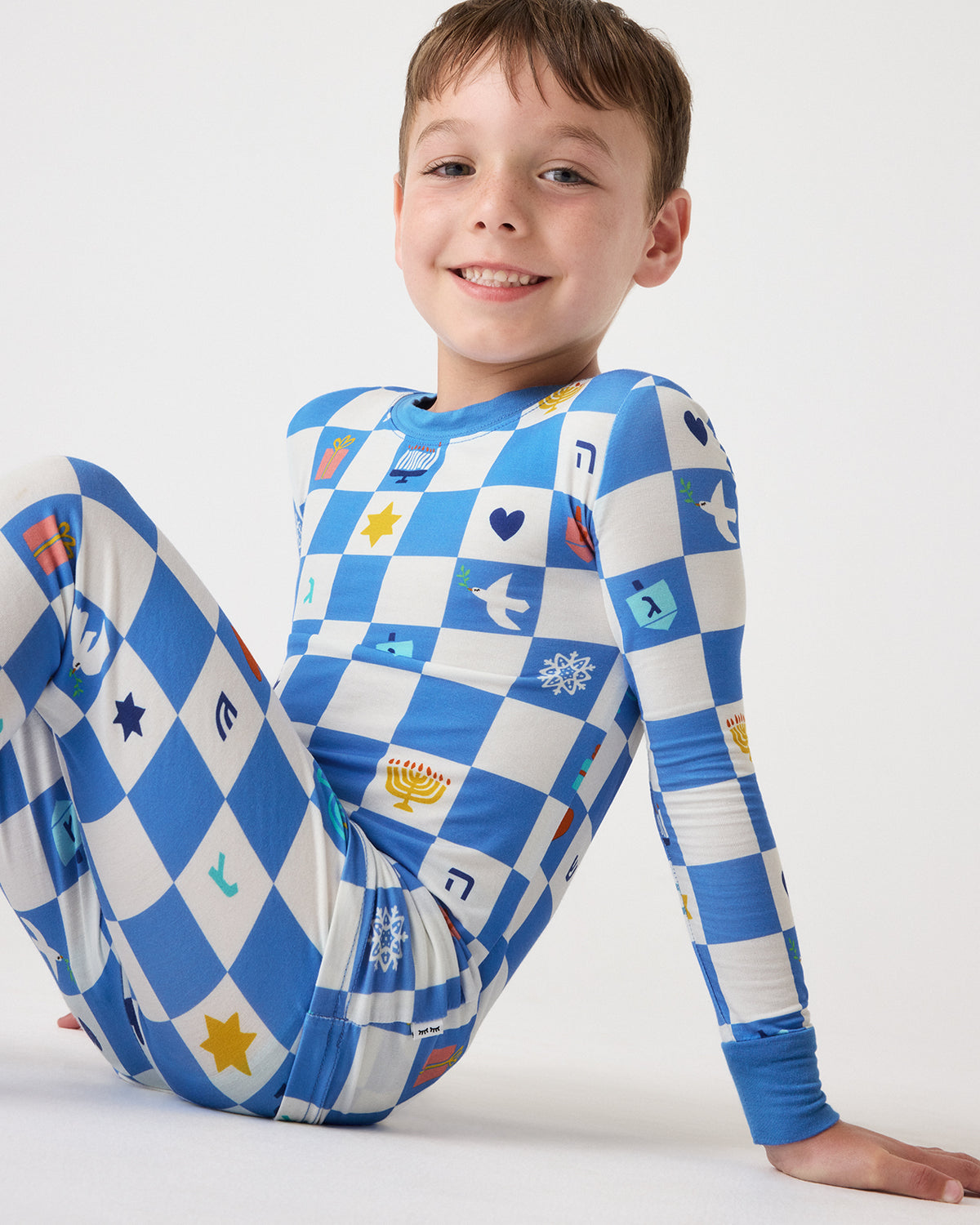 Sitting child wearing the Hanukkah Checks Two-Piece Pajama Set