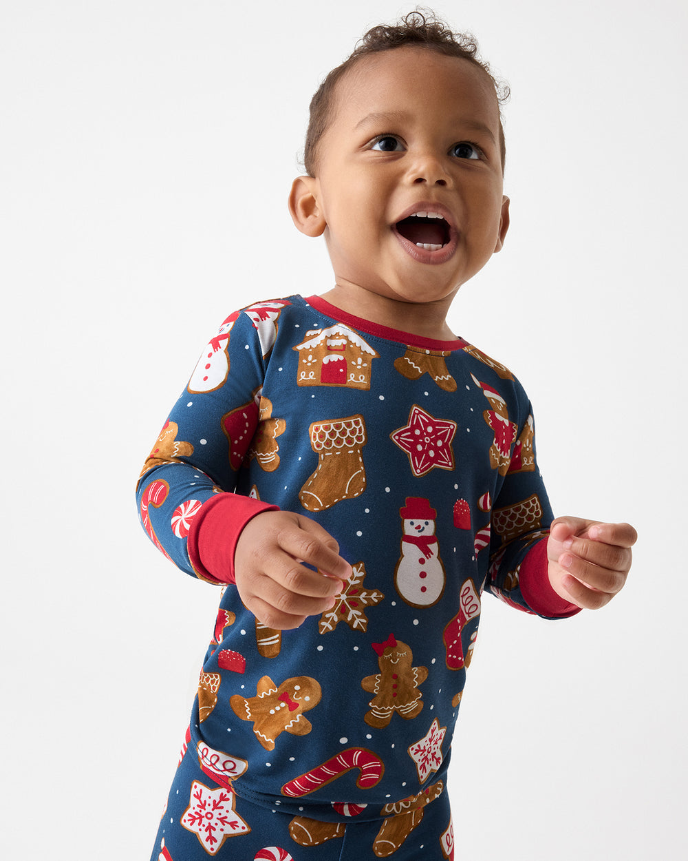 A toddler wearing a festive navy blue long-sleeve pajama with a Christmas gingerbread print, including snowmen, gingerbread cookies, candy canes, and stockings, posed against a clean white background.