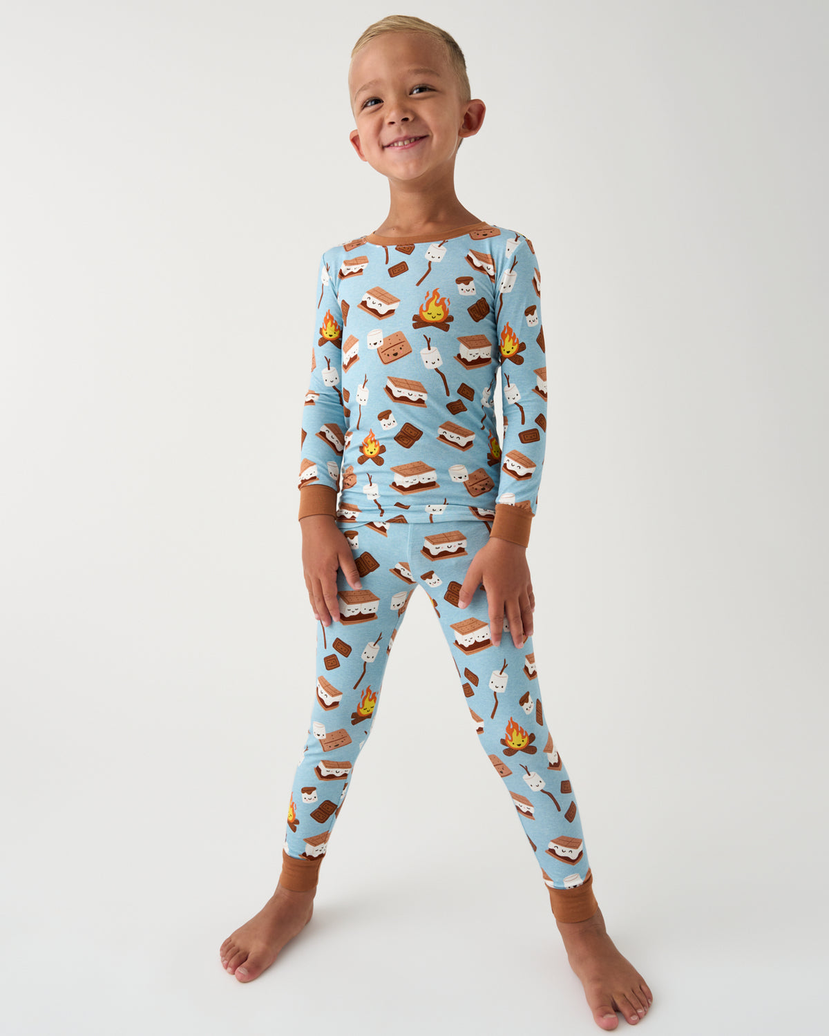 A young child modeling a light blue long-sleeve pajama set with a s'mores print, standing against a plain white studio background.