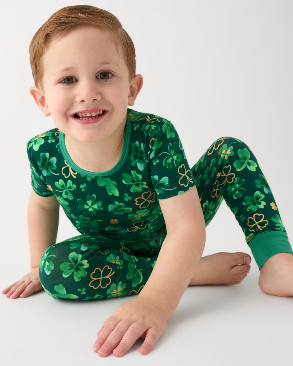 Sitting boy wearing the Clover Cuties Two-Piece Short Sleeve Pajama Set 