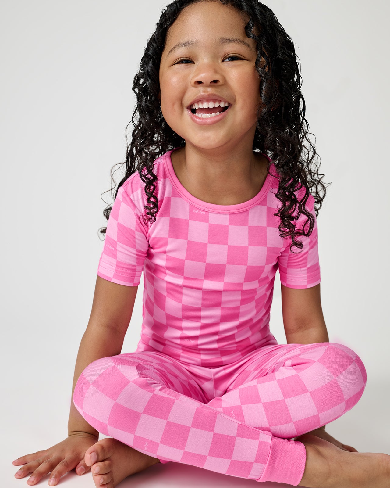 Sitting girl wearing the Sweet Raspberry Checks Two-Piece Short Sleeve Pajama Set