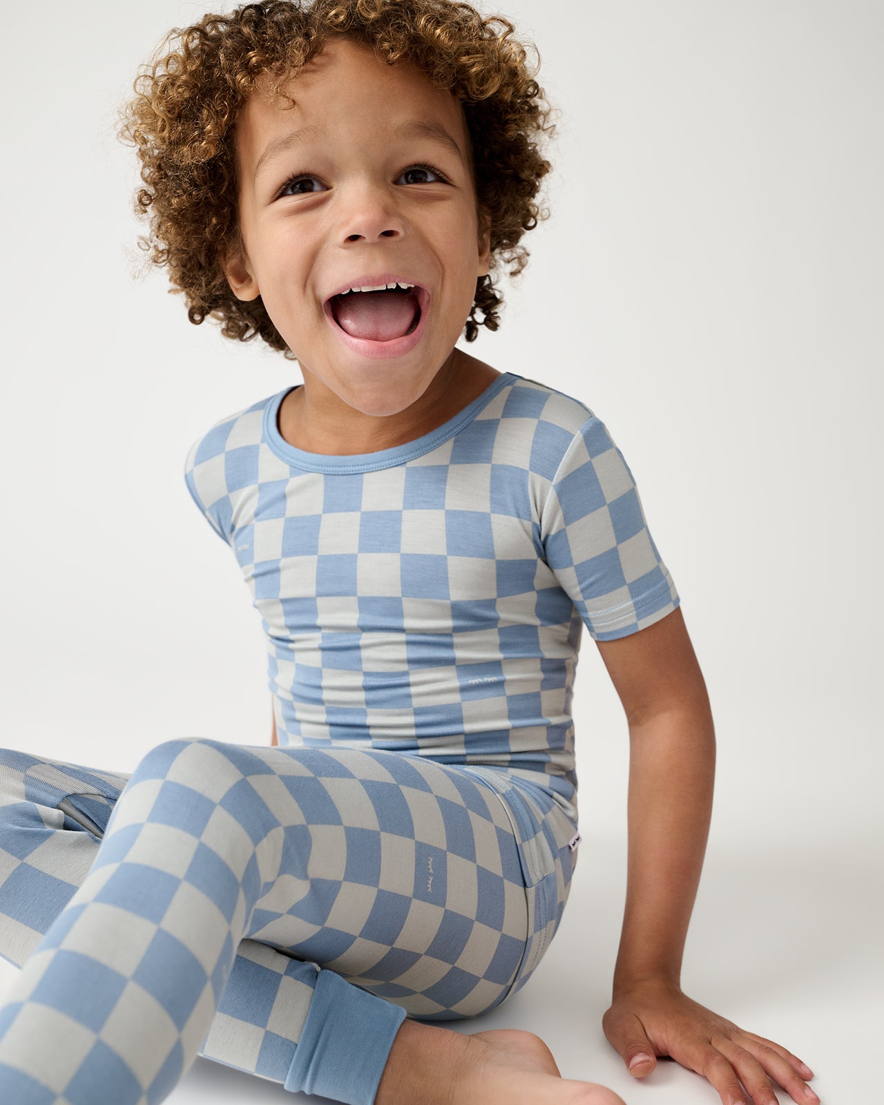 Sitting boy wearing the Dusk Blue Checks Two-Piece Short Sleeve Pajama Set