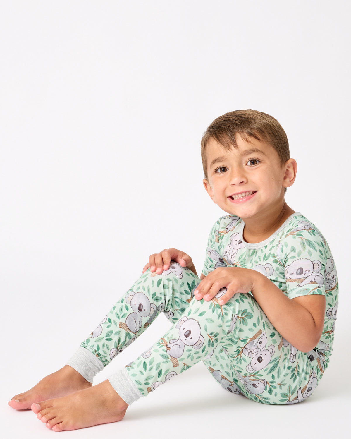 Sitting boy wearing the Koala Cuddles Two-Piece Short Sleeve & Pants Pajama Set