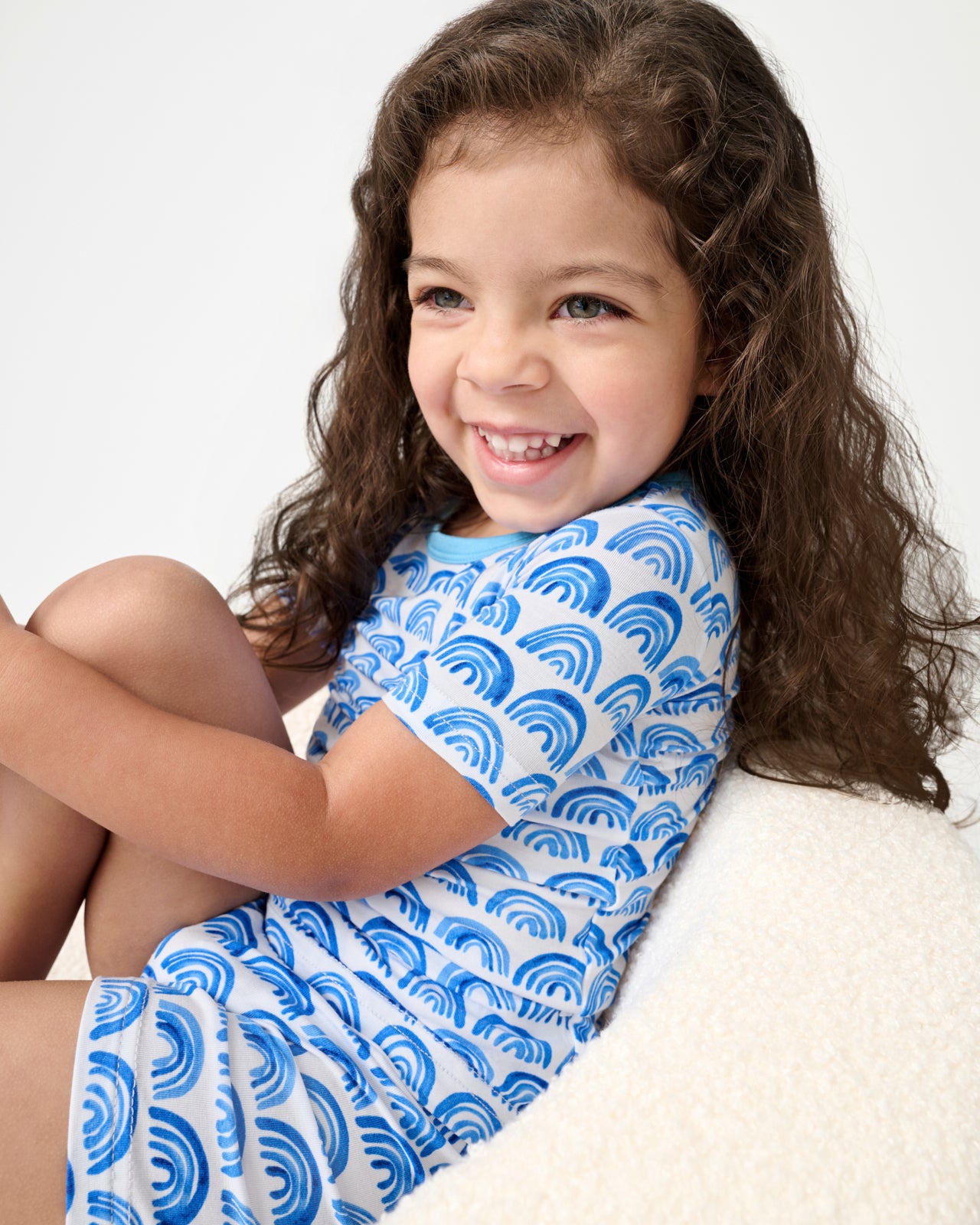 Sitting girl wearing the Blue Rainbows Two-Piece Short Sleeve & Shorts Pajama Set