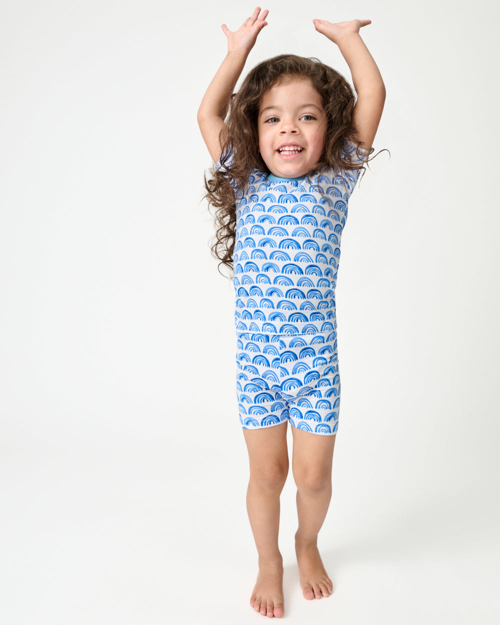 Standing girl wearing the Blue Rainbows Two-Piece Short Sleeve & Shorts Pajama Set