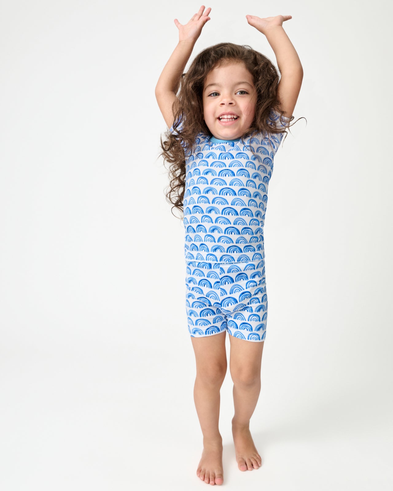 Standing girl wearing the Blue Rainbows Two-Piece Short Sleeve & Shorts Pajama Set