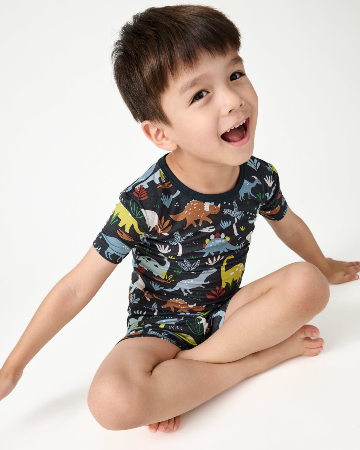 Sitting boy wearing the Navy Jurassic Jungle Two-Piece Short Sleeve & Shorts Pajama Set