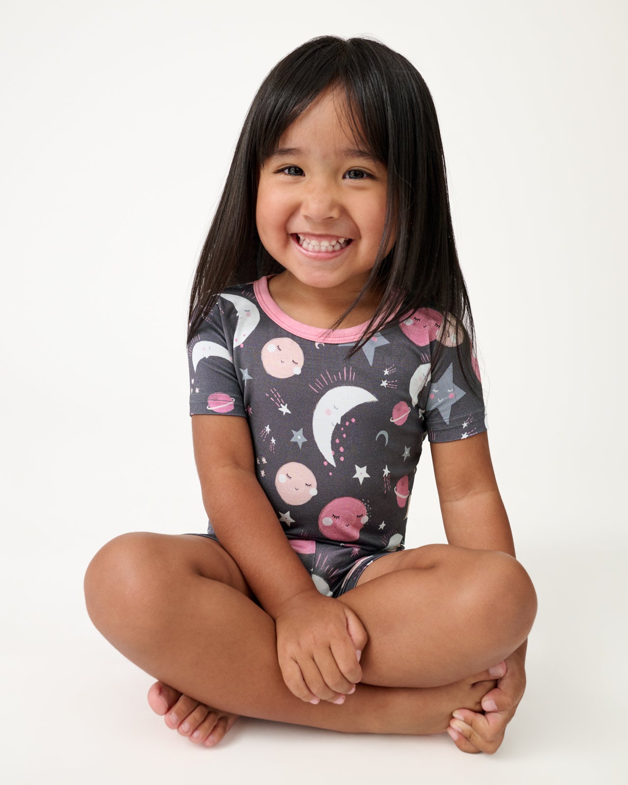Sitting girl wearing the Pink To the Moon & Back Two-Piece Short Sleeve & Shorts Pajama Set
