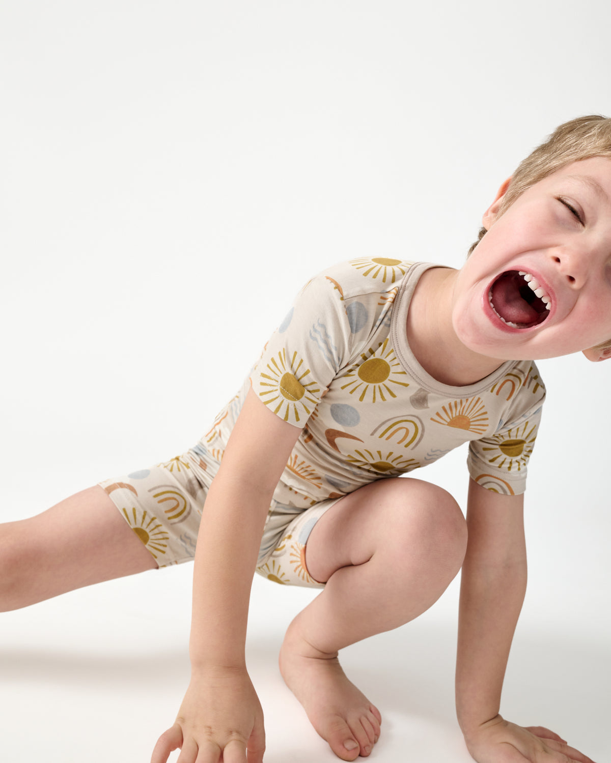 Close up of crouching boy wearing the Desert Sunrise Two-Piece Short Sleeve & Shorts Pajama Set