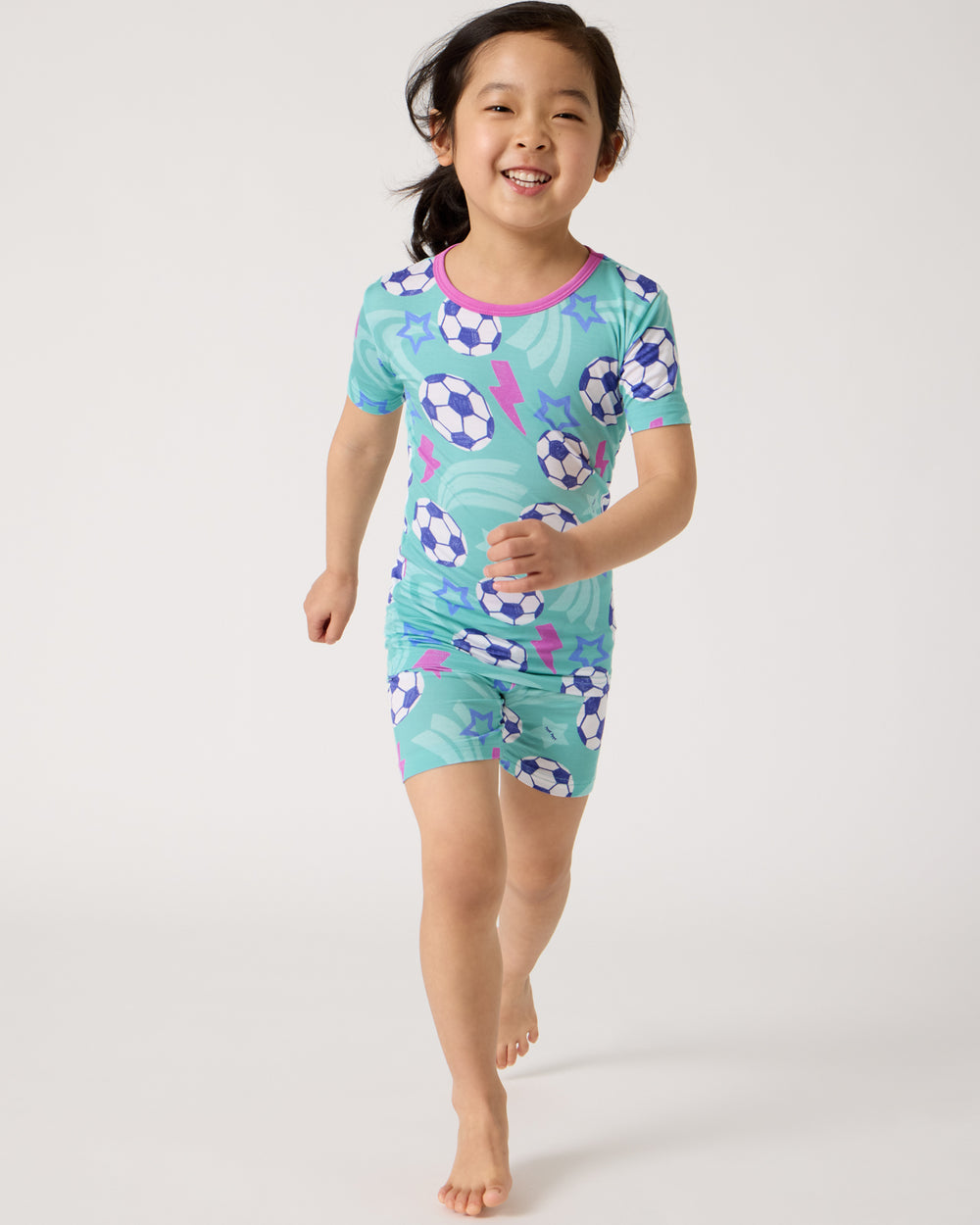 Running girl wearing the Aqua Soccer Stars Two-Piece Short Sleeve & Shorts Pajama Set