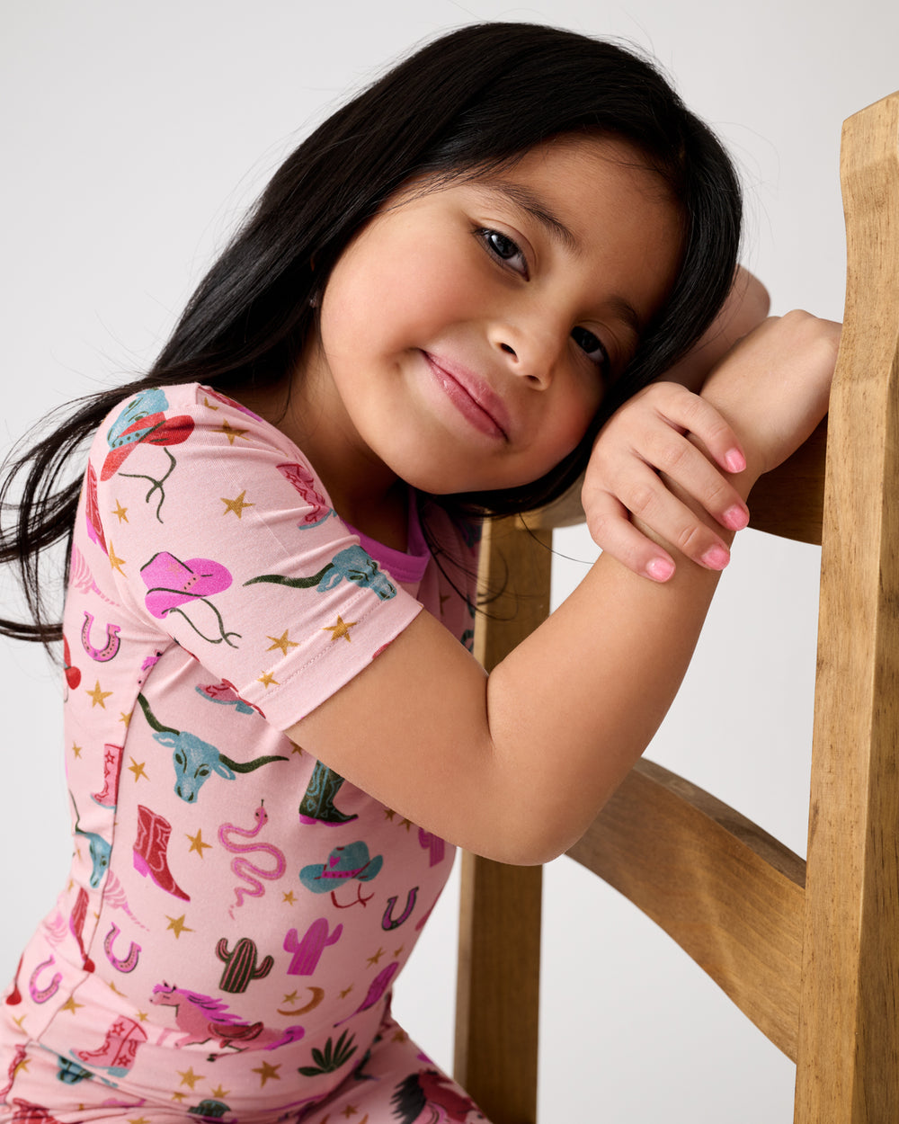 Close up of girl leaning on a chair wearing the Pink Rancher Roundup Two-Piece Short Sleeve & Shorts Pajama Set