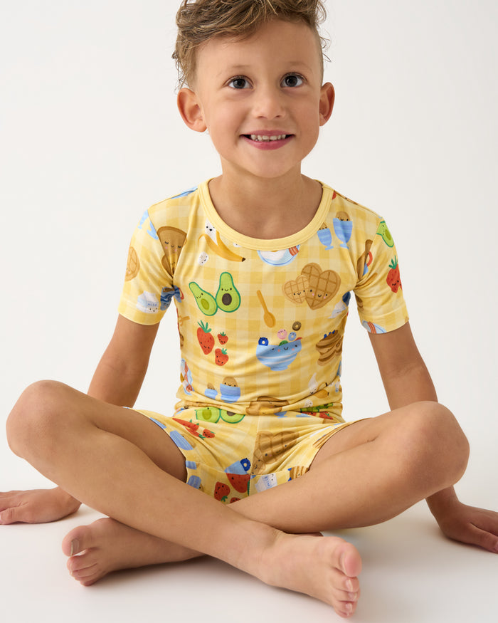 Sitting boy wearing the Breakfast Bunch Two-Piece Short Sleeve & Shorts Pajama Set