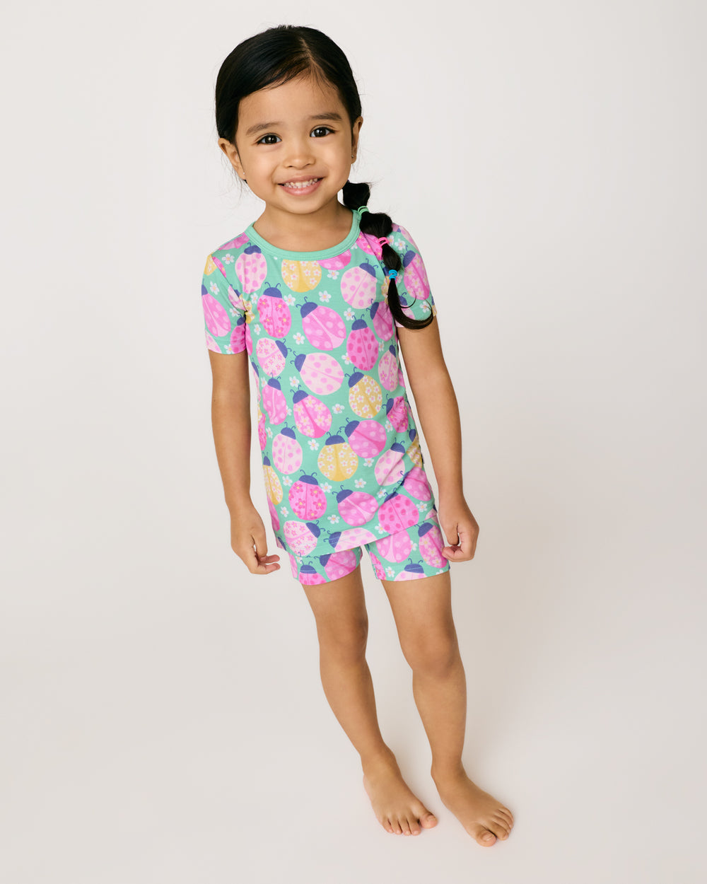 Standing girl wearing the Ladybug Meadow Two-Piece Short Sleeve & Shorts Pajama Set
