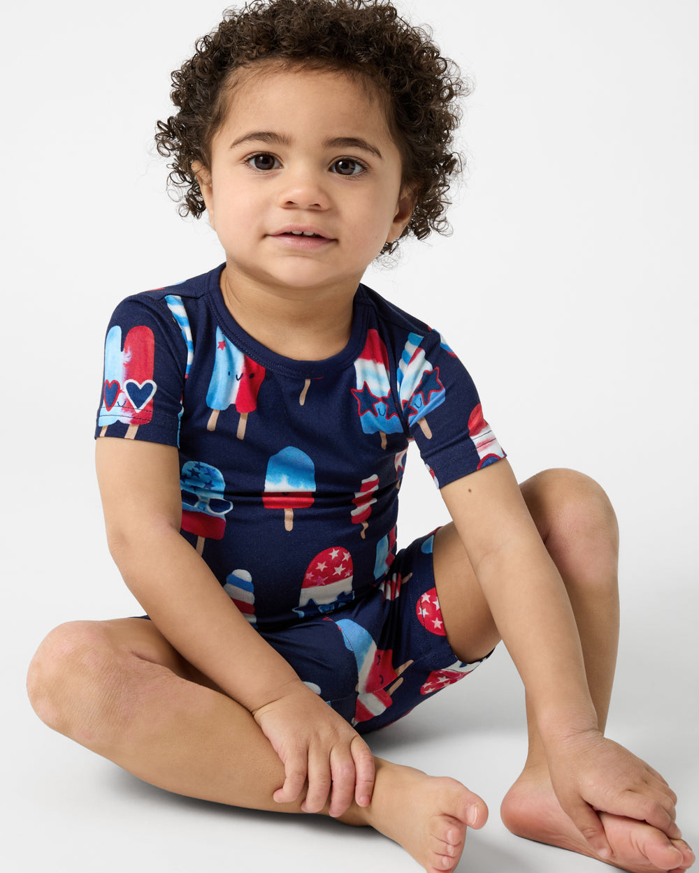 Sitting boy wearing the Sparkle Treats Two-Piece Short Sleeve & Shorts Pajama Set