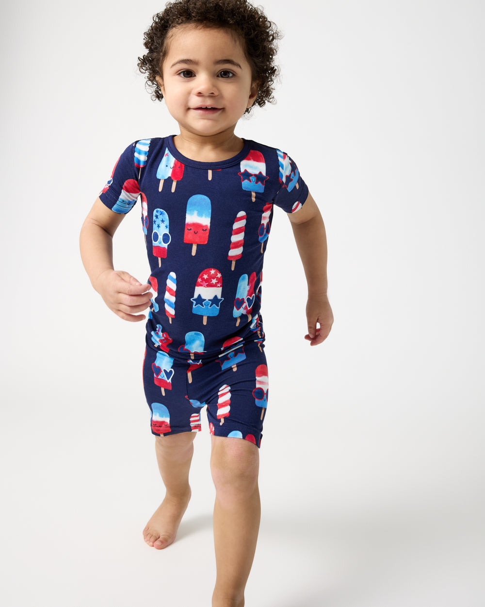 Walking boy wearing the Sparkle Treats Two-Piece Short Sleeve & Shorts Pajama Set