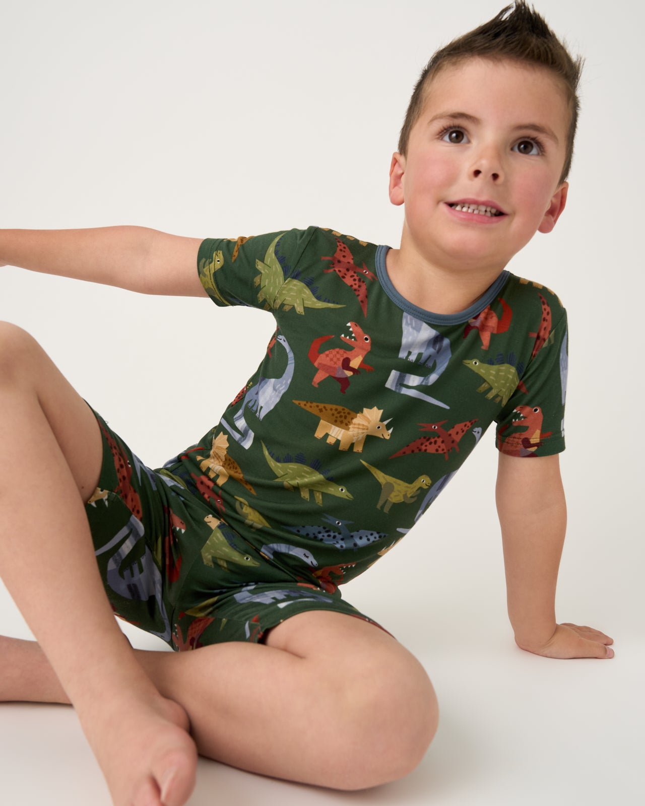 Sitting boy wearing the Green Roar & Explore Two-Piece Short Sleeve & Shorts Pajama Set