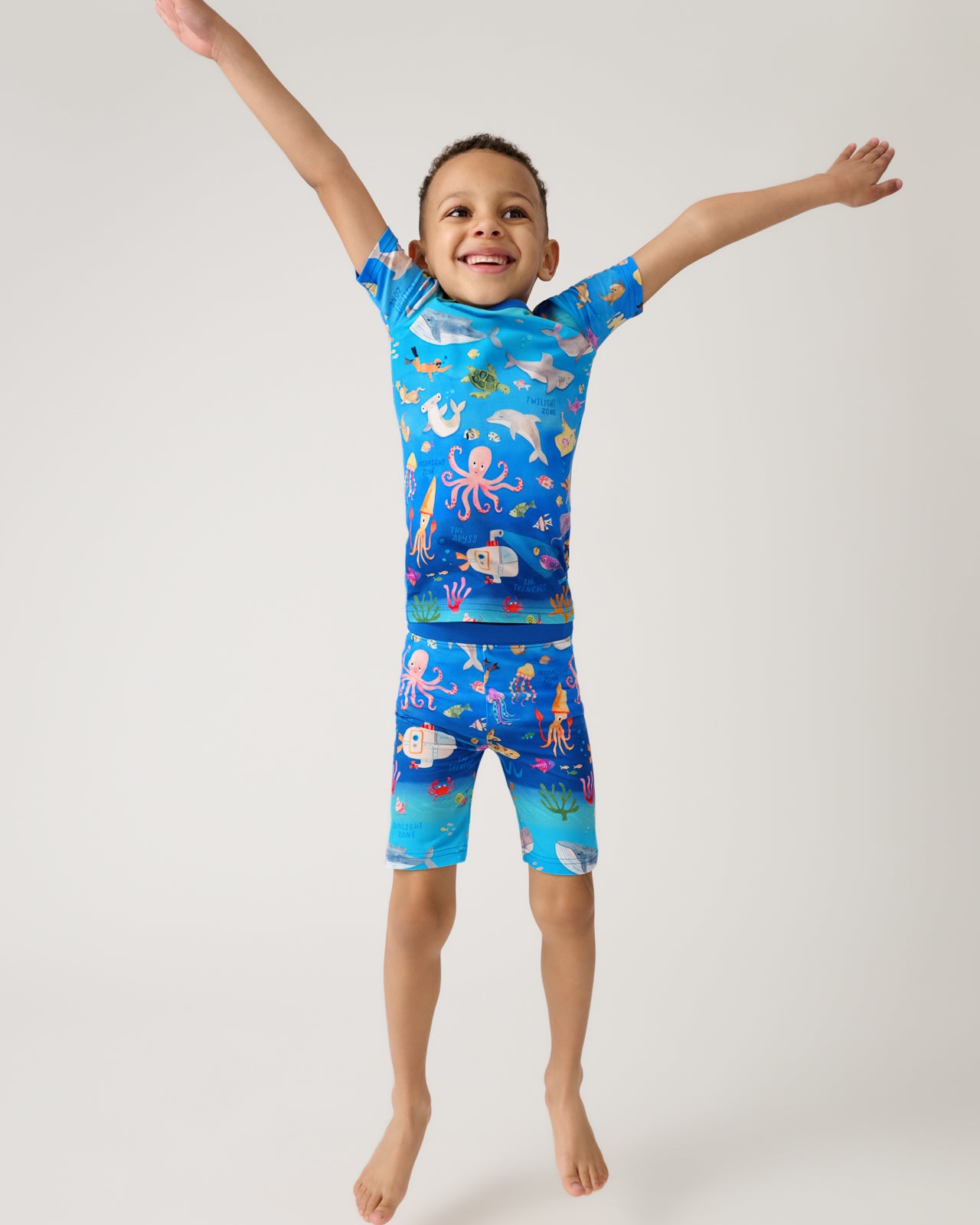 Jumping child wearing the Underwater Discovery Two-Piece Short Sleeve & Shorts Pajama Set