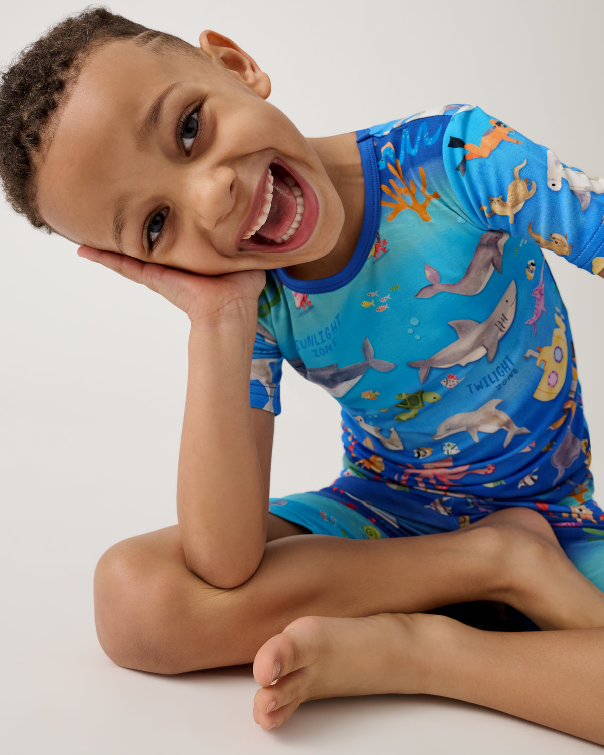 Sitting boy wearing the Underwater Discovery Two-Piece Short Sleeve & Shorts Pajama Set