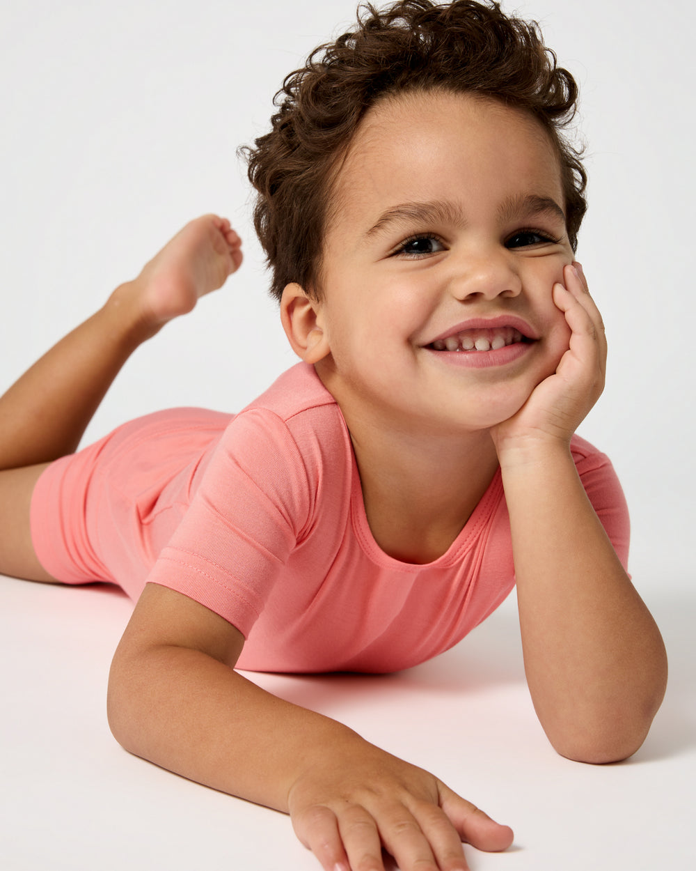 Child laying on a white surface wearing the Sweet Papaya Two-Piece Short Sleeve & Shorts Pajama Set